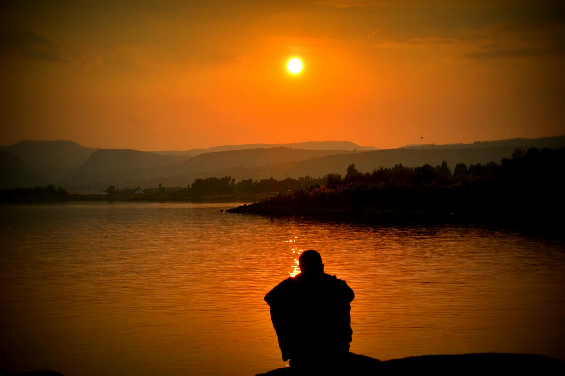 Person sitting by lake at sunset